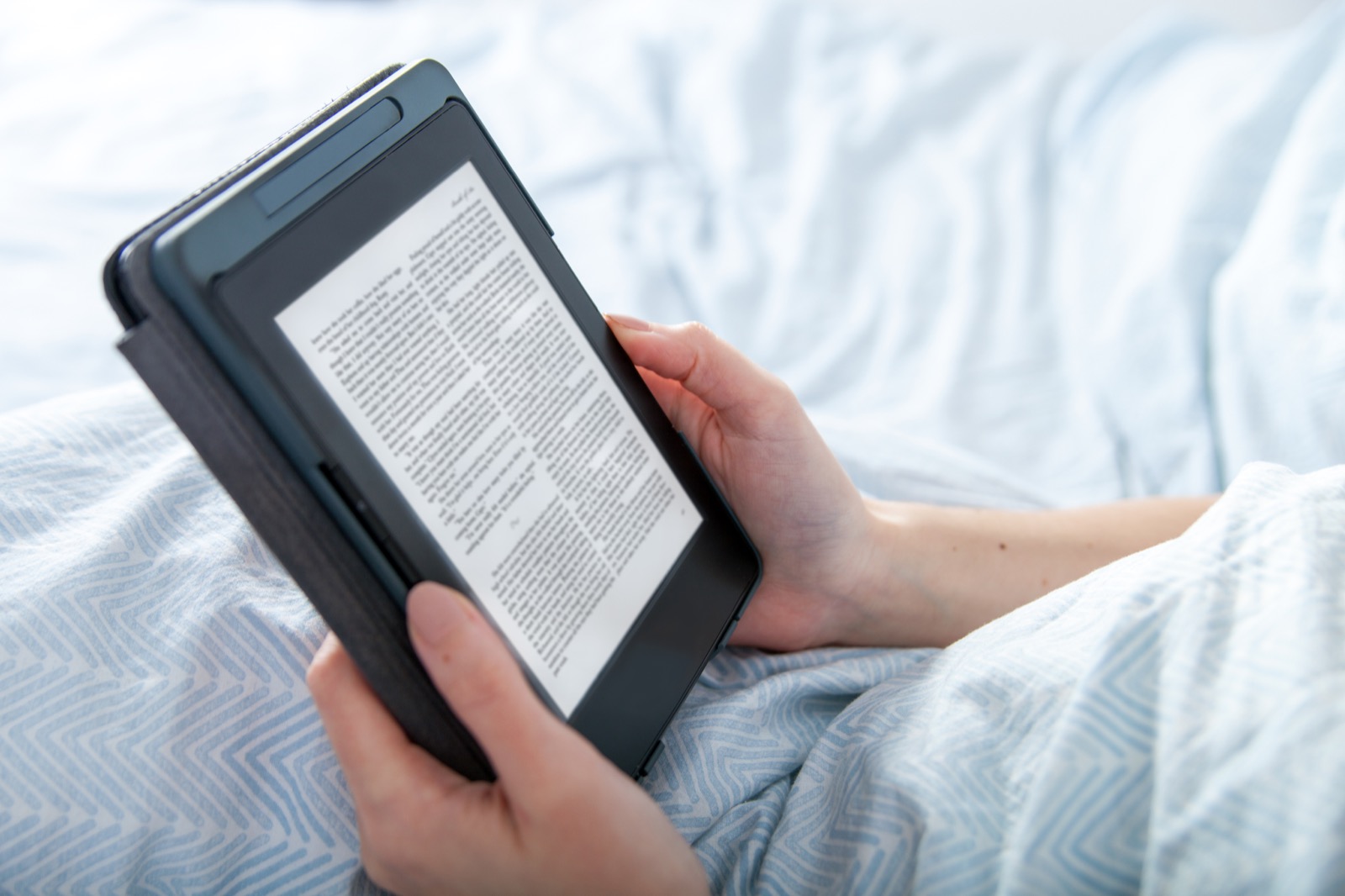 Hands holding an e-reader displaying a book